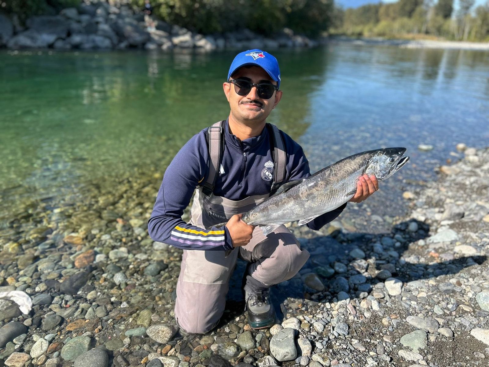 Aneesh kneeling by the riverbank with a silver salmon