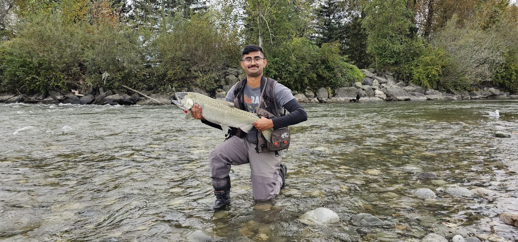 Aneesh kneeling in a BC river holding a large salmon